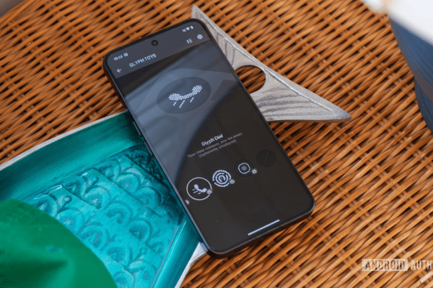 A black smartphone displaying the Glyph Toys app interface is positioned on a woven surface, with a teal object and a metallic decorative item nearby.