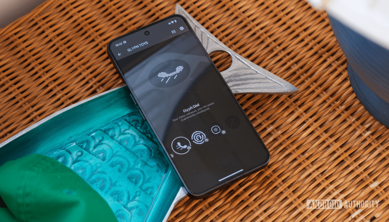 A black smartphone displaying the Glyph Toys app interface is positioned on a woven surface, with a teal object and a metallic decorative item nearby.