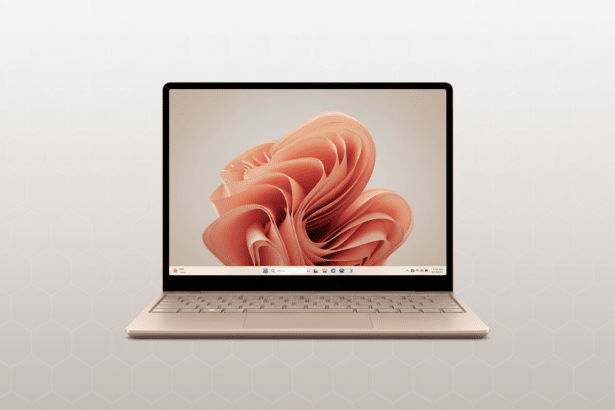 A gold laptop with a coral - colored, abstract floral background on the screen, set against a subtle gray geometric pattern.