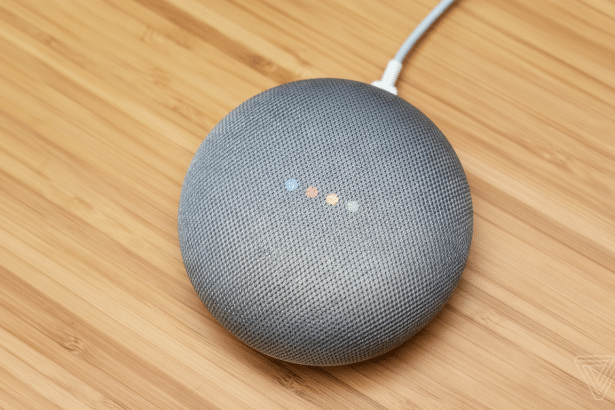 A grey Google Home Mini smart speaker with four colored lights on top, resting on a wooden surface.