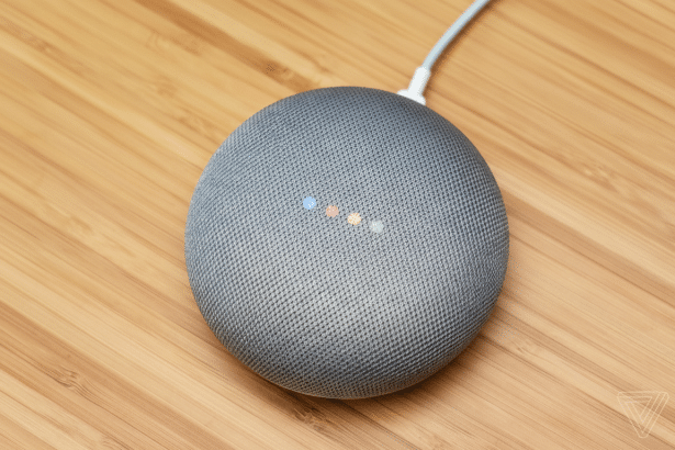 Google Nest Mini smart speaker on a wooden surface, showing its colored indicator lights. Filename :