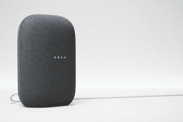 A dark gray Google Nest Audio smart speaker with a white power cord extending to the right, presented against a clean white background. Filename : googlenest audiospeaker .png