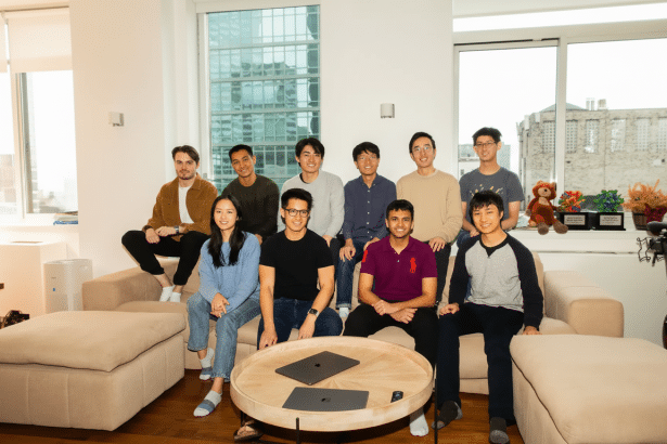 A group of ten young individuals, predominantly male, posing together in a modern, well -lit living room. They are casually dressed and are seated and