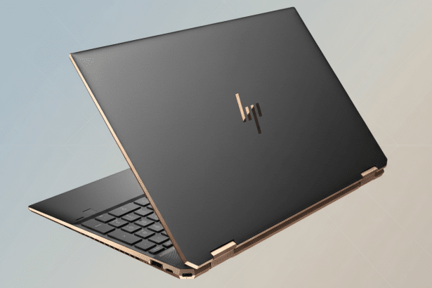 An HP Spectre laptop with a dark gray lid and gold accents, slightly open, on a soft gradient background.