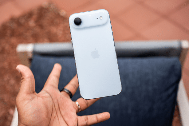 A hand holding a white iPhone 14, with the back visible , against a blurred outdoor background.