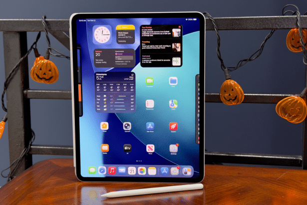 An iPad displaying various widgets and apps, set on a wooden table with Halloween pumpkin lights in the background.