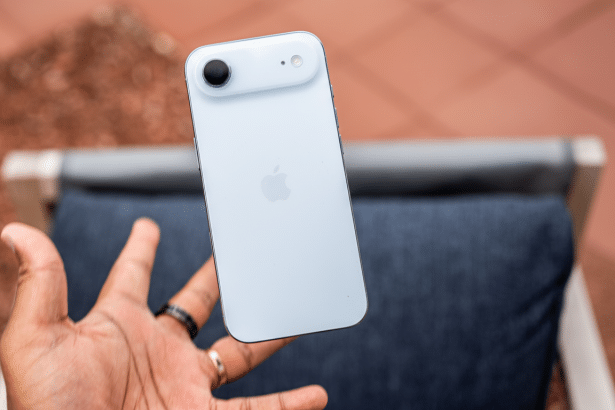 A hand holding a white iPhone 15, showcasing the back of the phone with its single camera and Apple logo .