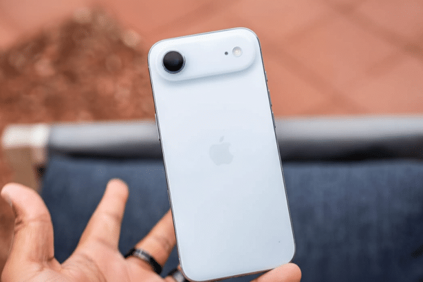 A hand holding a white iPhone, viewed from the back, against a blurred reddish -brown and blue background.