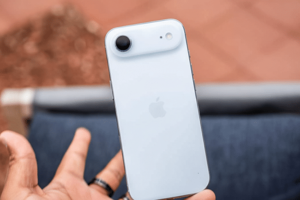 A hand holding a white iPhone SE with the Apple logo visible, against a blurred reddish -brown and blue background.