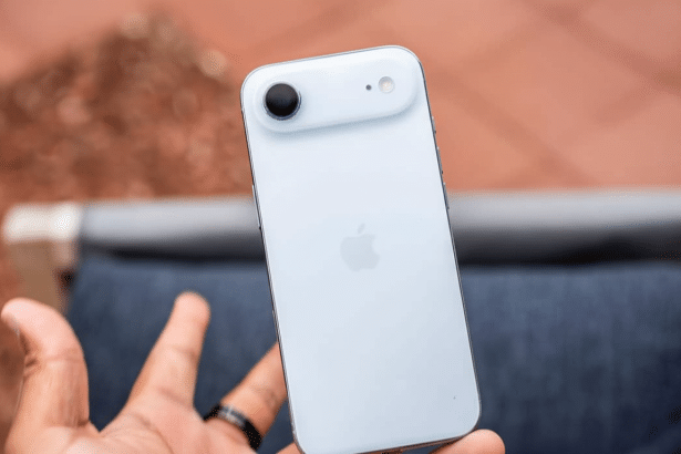 A hand holding a white smartphone with the Apple logo visible on the back, shown against a blurred reddish -brown and blue background.
