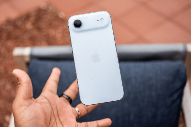 A hand holding a light blue iPhone with the Apple logo visible, against a blurred background of a red tiled surface and a gray cushion.
