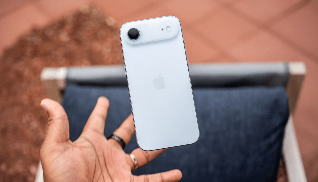 A hand holding a light blue iPhone with the Apple logo visible, against a blurred background of a red tiled surface and a gray cushion.