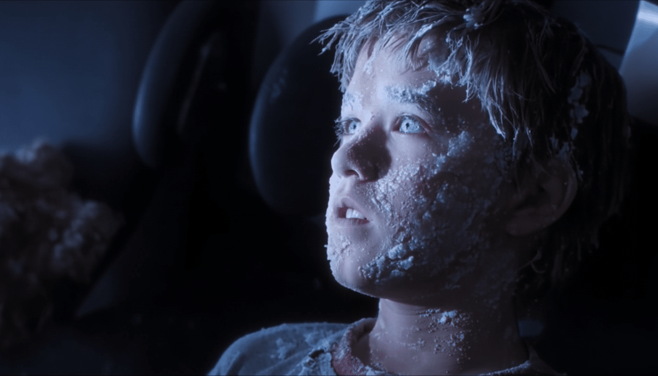 A young boy with a pale , snow -covered face and glowing blue eyes looks upwards in a dimly lit setting .