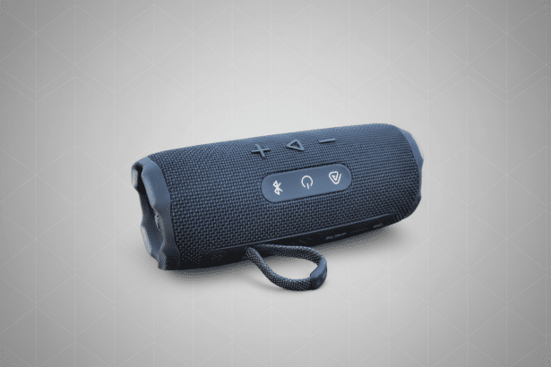 A black JBL Flip 5 portable Bluetooth speaker on a grey background with a subtle geometric pattern.