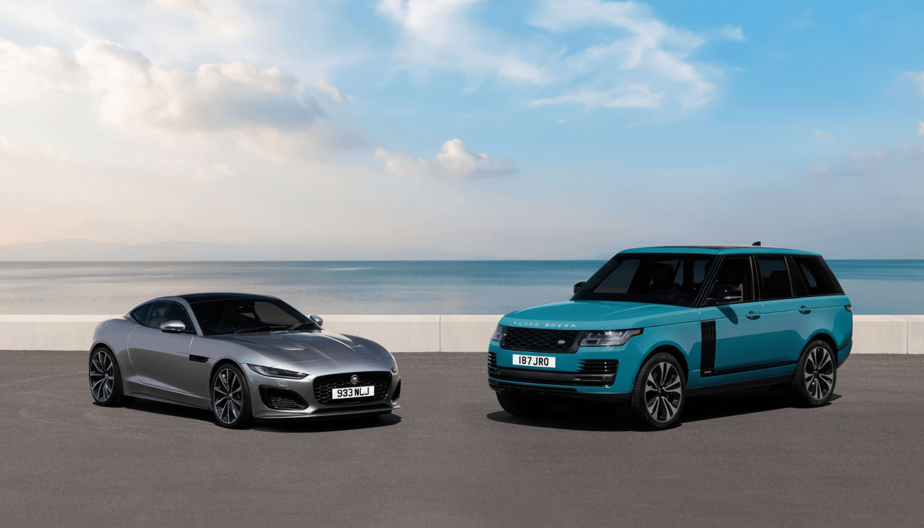 A silver Jaguar F- Type coupe and a teal Range Rover SUV parked side-by- side on an asphalt road with the ocean and a partly cloudy sky in the backgro