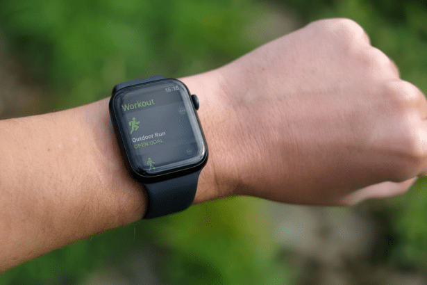 A close -up shot of a persons wrist wearing an Apple Watch, displaying the Workout app with Outdoor Run and Open Goal selected. The background is a na