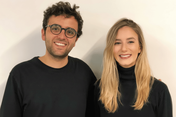 Two smiling individuals , a man and a woman, standing against a white background , resized to a 16: 9 aspect ratio.