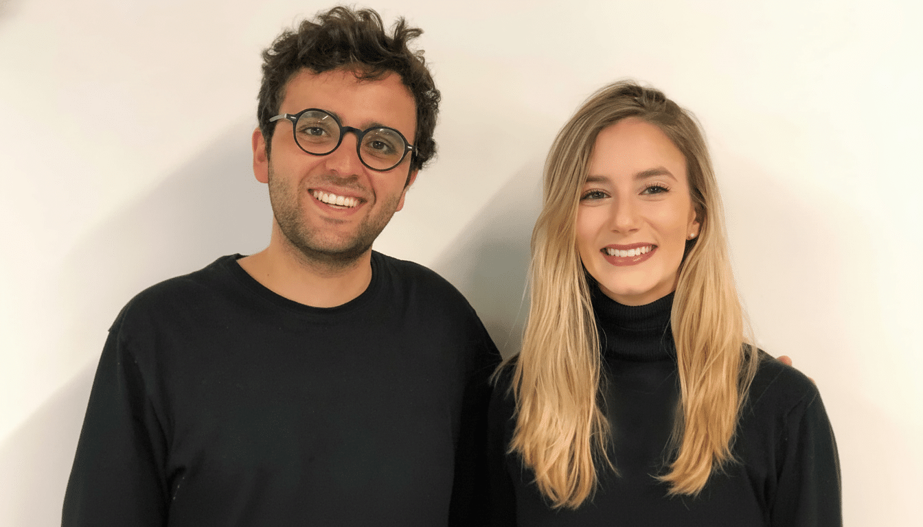 Two smiling individuals , a man and a woman, standing against a white background , resized to a 16: 9 aspect ratio.