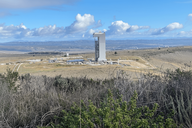 alt text: A launch tower stands tall in the middle of a vast , open landscape under a blue sky with
