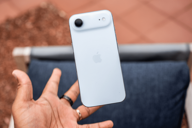 A hand holding a light blue iPhone against a blurred outdoor background.