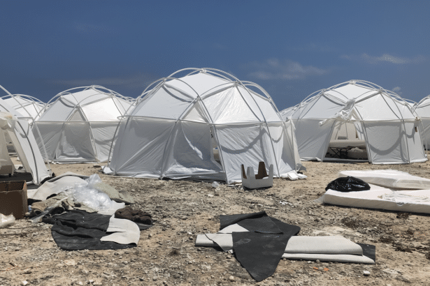 Several white geodesic dome tents set up on a rocky , barren landscape under a clear blue sky, with some scattered debris in the foreground.