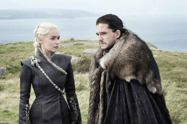 Da enerys Targary en and Jon Snow stand on a grassy cliff overlooking the sea , looking at each other intensely .