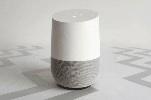 A white and grey smart speaker with colorful indicator lights on top, set against a simple white background with faint zigzag patterns.