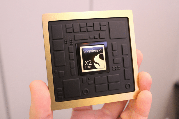 A hand holds a gold and black Snapdragon X2 Elite chip, with the logo visible in the center.