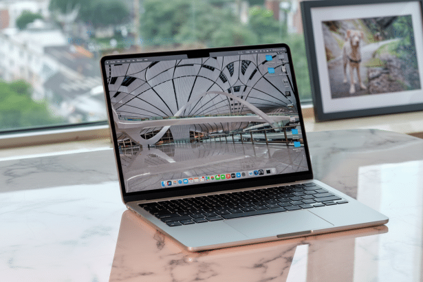 A silver MacBook Pro laptop displayed on a marble surface with a blurred outdoor background and a framed picture of a dog.