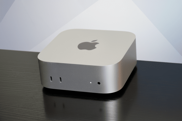 A silver Apple Mac Mini on a dark wooden surface with a professional light gray and white patterned background, resized to a 16: 9 aspect ratio.