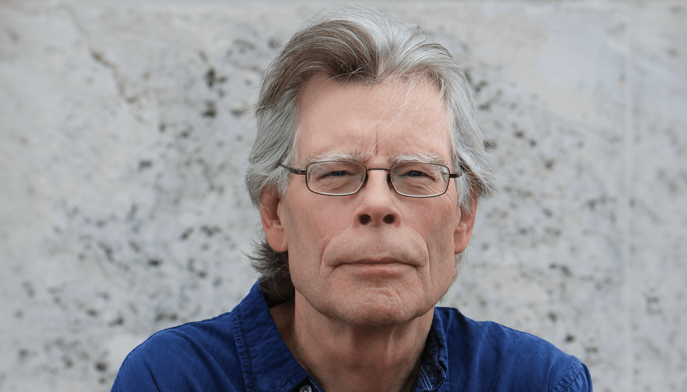 A close- up, professionally enhanced portrait of a man with gray hair and glasses, wearing a blue shirt, looking directly at the viewer with a neutral expression, against a light gray textured background .