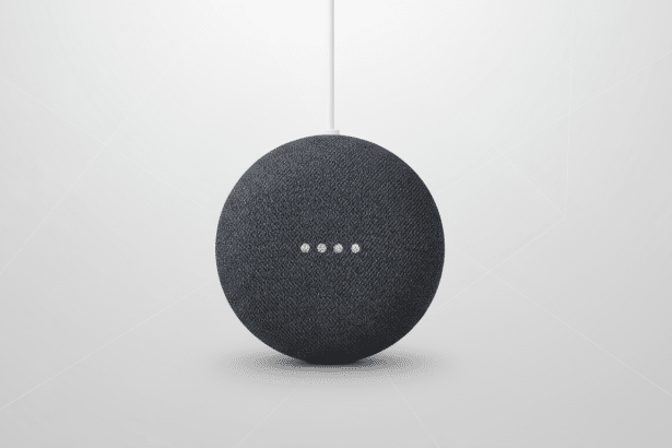 A dark gray Google Home Mini smart speaker with a white cable extending upwards , centered on a light gray background with subtle geometric patterns. Filename : googlehome minienhanced . png