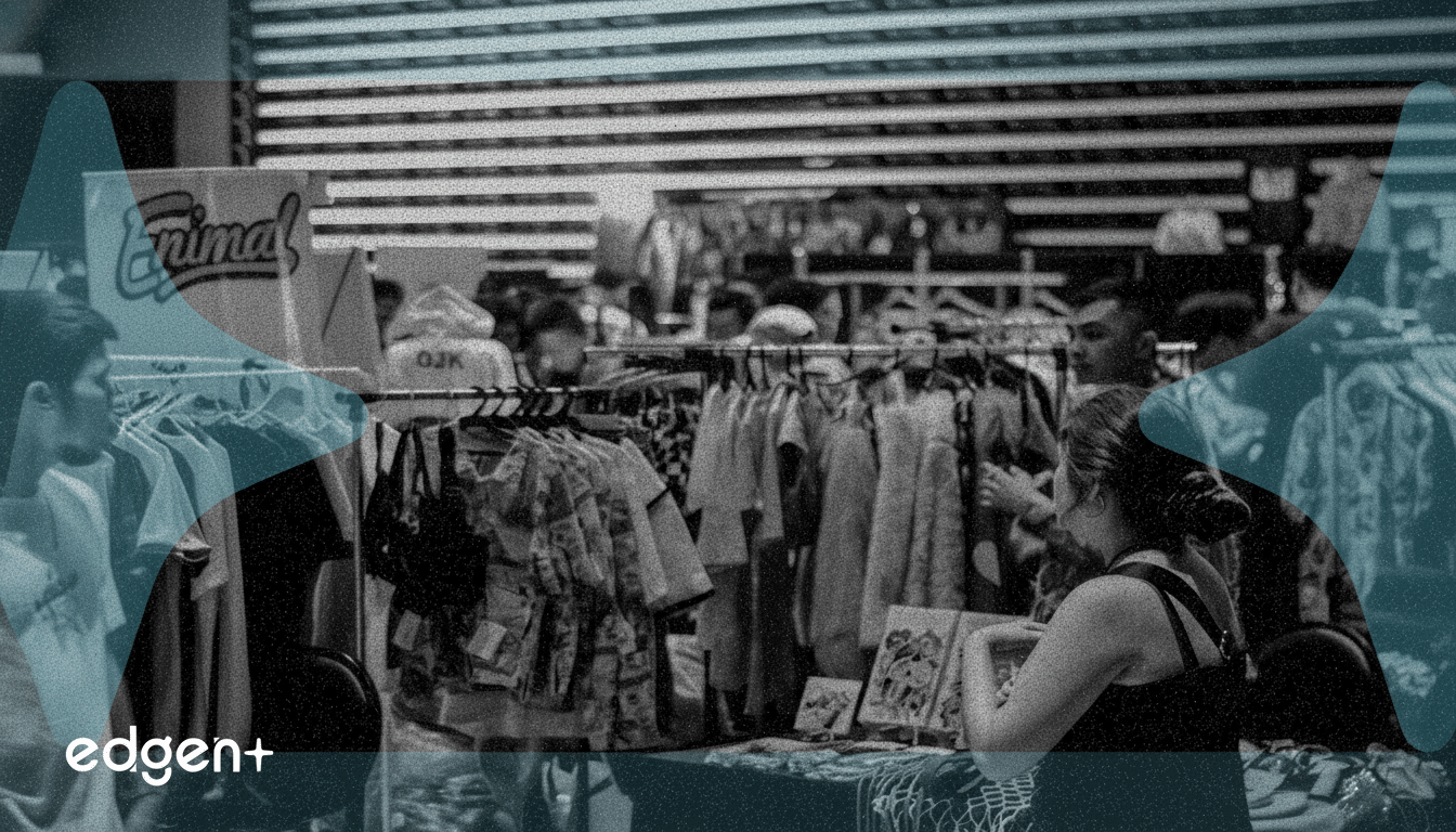 A black and white image of a bustling market scene with racks of clothes and people browsing, overlaid with a translucent blue abstract shape and the  edgen+ logo in the bottom left corner .