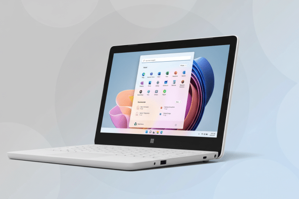 A white laptop with a minimalist design displays a colorful Windows operating system interface with app icons and a search bar, set against a subtle gray -blue gradient background with soft circular patterns. Filename : white laptopwindows interface. png