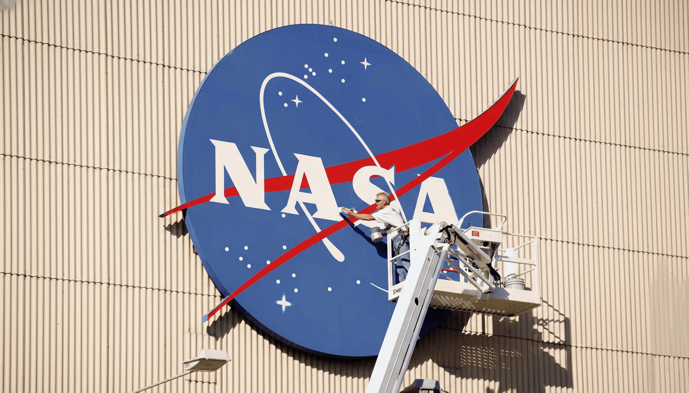 A man in a cherry picker cleaning a large NASA logo on the side of a building .