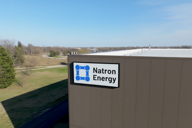 The Natron Energy sign is affixed to the side of a modern building , with a clear blue sky overhead and green landscape visible in the background.