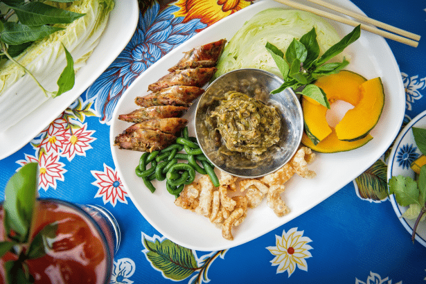 An overhead shot of a platter of Northern Thai food with various components, including sai o ua (Thai sausages), nam pri k no om (green chili dip), cr