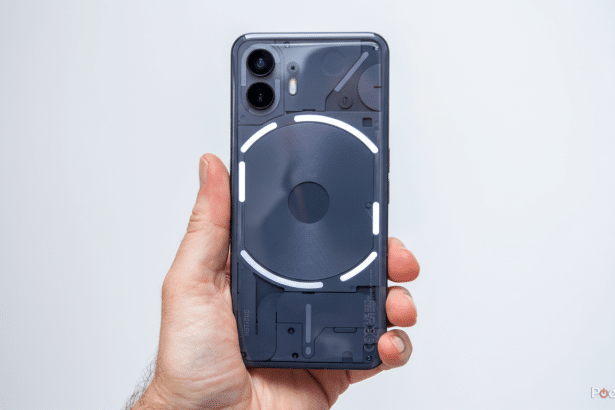 A hand holds a Nothing Phone (1) with its Glyph Interface glowing, set against a plain white background, resized to a 16: 9 aspect ratio.