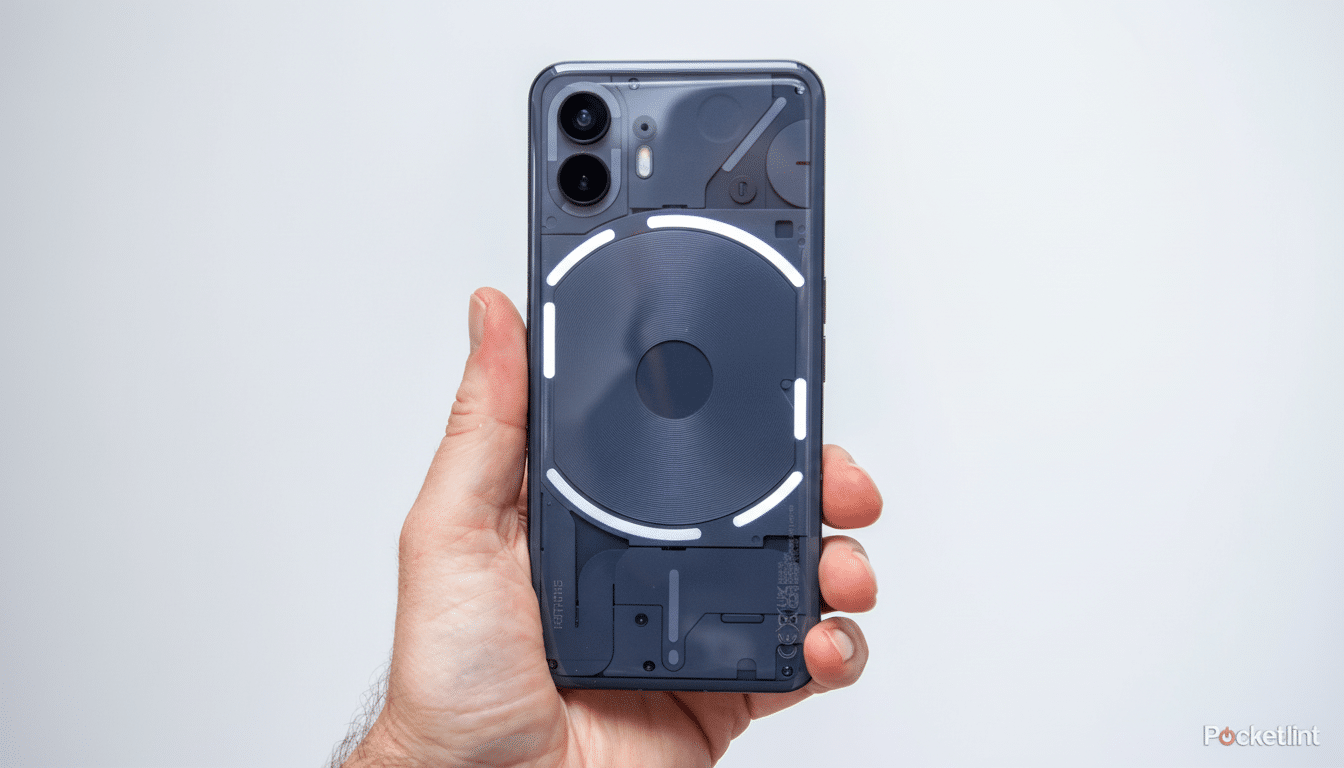 A hand holds a Nothing Phone (1) with its Glyph Interface glowing, set against a plain white background, resized to a 16: 9 aspect ratio.