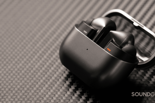 A pair of black wireless earbuds in an open charging case, resting on a dark gray textured surface.