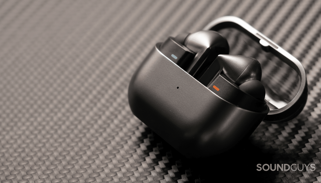 A pair of black wireless earbuds in an open charging case, resting on a dark gray textured surface.