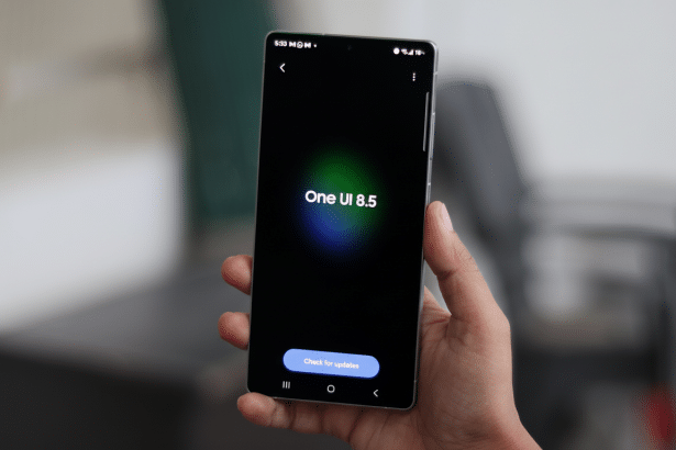 A hand holding a smartphone displaying One UI 8 .5 and a Check for updates button on a dark screen , with a blurred background. Filename : smartphone oneui 8. 5update . png