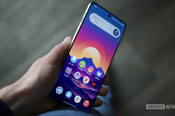 alt = A hand holds a smartphone displaying a colorful sunset wallpaper and various app icons on its