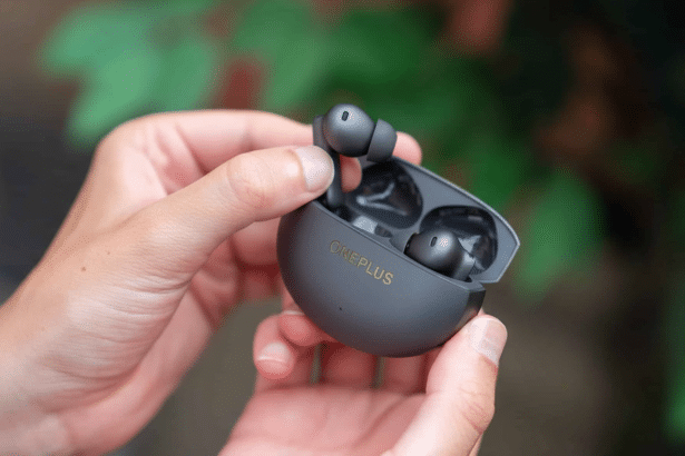 A pair of black OnePlus wireless earbuds in their charging case, held open by two hands, with a green, leafy background.