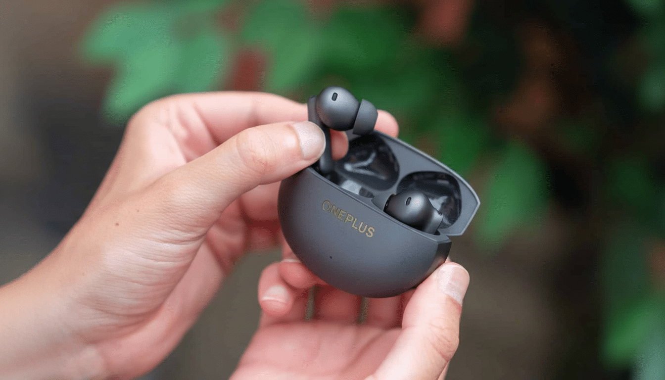 A pair of black OnePlus wireless earbuds in their charging case, held open by two hands, with a green, leafy background.