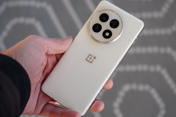 A hand holding a white OnePlus smartphone , showing its rear camera module and the OnePlus logo. Filename : oneplus phone held 16 9.png