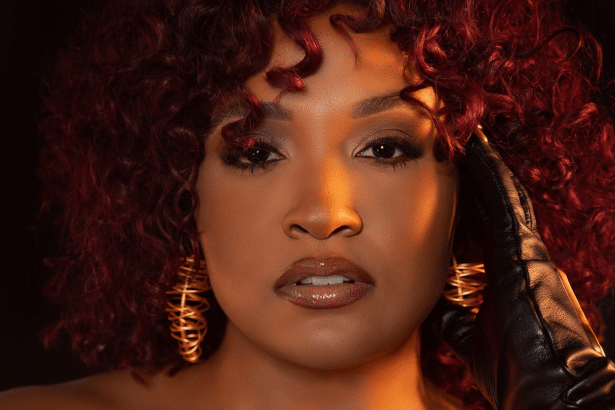 A professional head shot of a woman with red curly hair and gold earrings, wearing a black glove, against a dark background, resized to 1 6:9 aspect ratio. Filename : professional headshot womanred hair. png