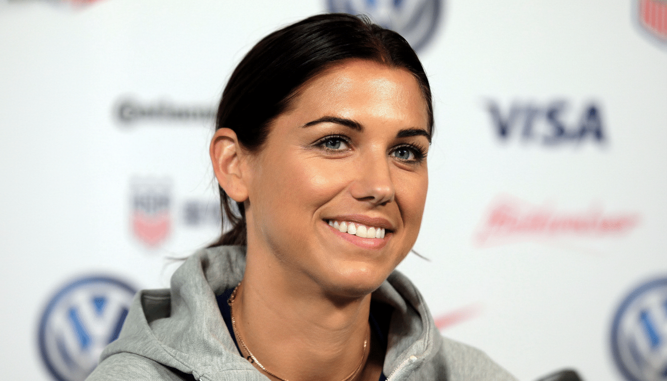 A professional head shot of a smiling woman with dark hair and blue eyes, wearing a gray hoodie and a gold necklace .