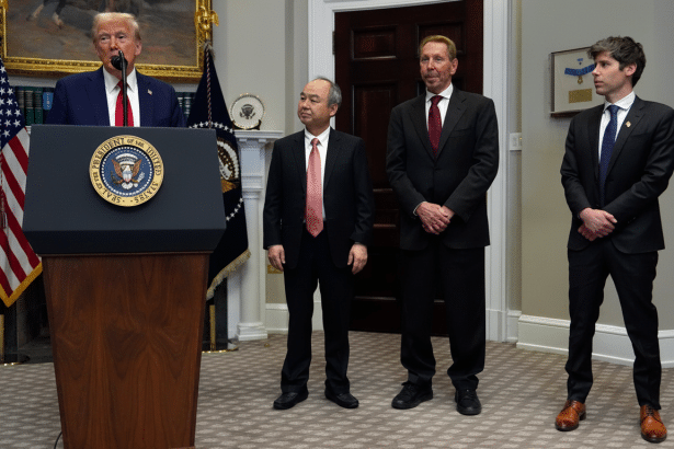 Donald Trump speaking at a podium with three other men standing to his right in a formal room .