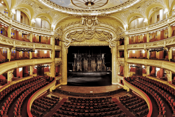 An ornate, historic opera house interior with empty red velvet seats and a grand stage.